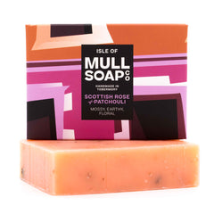 a Scottish rose and patchouli soap box sitting on the pink soap bar. The box is a pink colourful design. The soap is described as mossy, earthy and floral. Handmade in Tobermory by the Isle of Mull soap co.  